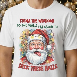 May include: White t-shirt featuring a colorful Santa Claus graphic with the text "From the windows to the walls I'm about to Deck These Halls." The Santa illustration includes a red hat, white beard, and a playful expression. The shirt is a festive holiday item.