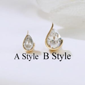 May include: Two gold-coloured teardrop-shaped earrings with clear, sparkling stones. The earrings are labelled "A Style" and "B Style" in black text. The background is a soft, neutral white.