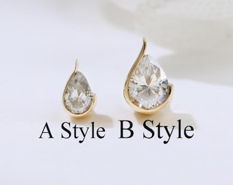 Könnte beinhalten: Zwei goldfarbene, tropfenförmige Ohrringe mit klaren, funkelnden Steinen. Die Ohrringe sind mit "A Style" und "B Style" in schwarzem Text beschriftet. Der Hintergrund ist ein weiches, neutrales Weiß.