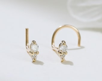 May include: Two gold nose studs with clear gemstones. One stud is a straight post, the other is a curved post. Each stud features a central marquise-cut stone and two smaller round stones. The jewelry is set against a white background.