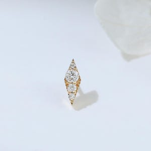 May include: A gold earring with a diamond-shaped design. The earring features a series of small, sparkling diamonds set in a linear pattern. The diamonds are clear and reflect light. The earring is set against a white background. A delicate piece of jewellery.