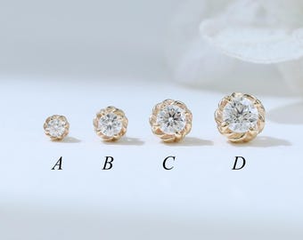 May include: Four gold-colored stud earrings with clear, round gemstones. Each earring has a different size, labeled A through D. The earrings are set against a soft, white background with a blurred floral element.