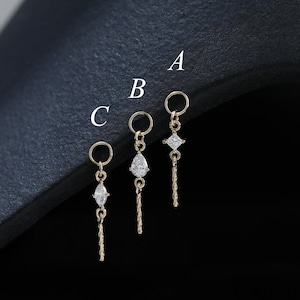 May include: Three gold-toned charms labeled A, B, and C, each featuring a small circular jump ring, a single clear gemstone, and a short textured vertical bar. Charm A has a square stone, B has a pear-shaped stone, and C has a marquise stone.