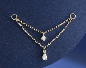 May include: A delicate gold chain with two dangling diamond charms. The chain is layered and features a small round diamond and a larger pear-shaped diamond.