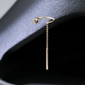 May include: A delicate gold earring featuring a small ball and a dangling rectangular bar. The earring is attached to a curved wire that fits through the ear. The design is simple and elegant.
