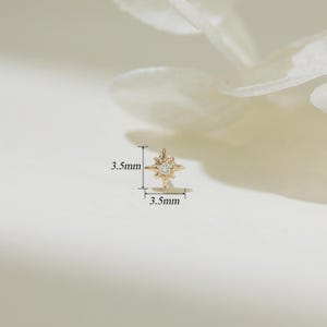 May include: A gold star-shaped earring with a small clear stone in the center. The earring measures 3.5 mm in diameter.