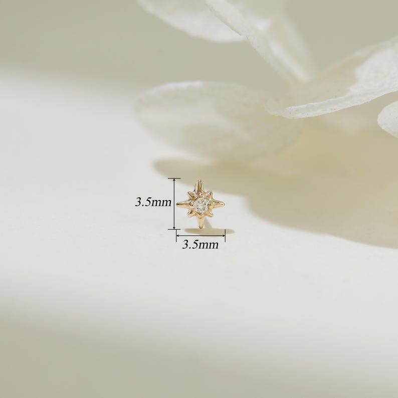 May include: A gold star-shaped earring with a small clear stone in the center. The earring measures 3.5 mm in diameter.