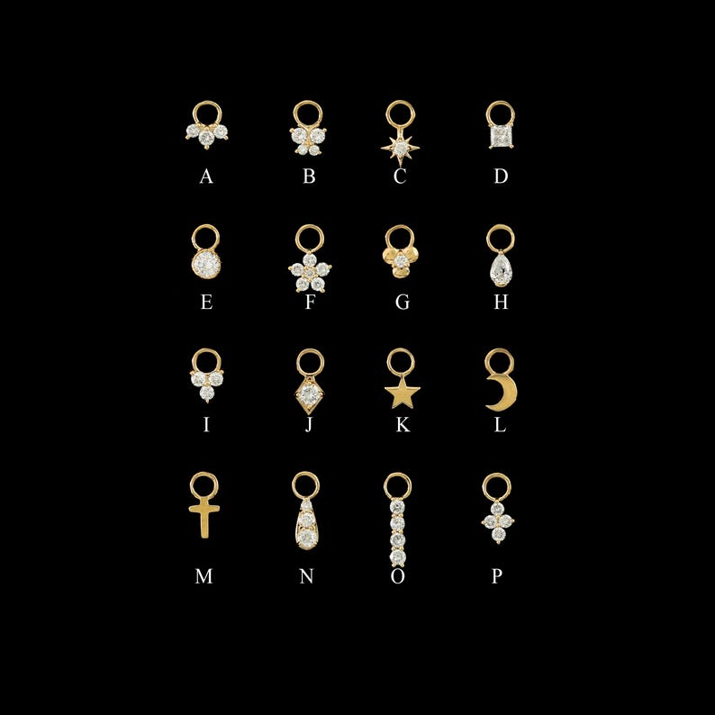 May include: A collection of gold-colored charms, each featuring a unique design. The charms include shapes like a bow, star, flower, moon, cross, and teardrop, all adorned with small, sparkling embellishments. Each charm is labeled with a letter from A to P, showcasing a variety of styles suitable for jewelry design.