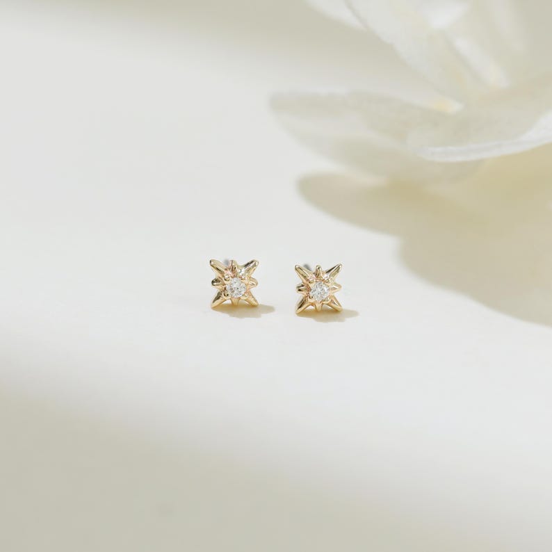 May include: A pair of gold star-shaped earrings with a small clear stone in the center of each star.