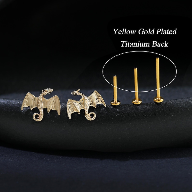 Puede incluir: Pendientes de drag&oacute;n chapados en oro y tres pendientes de bot&oacute;n dorados con parte trasera de titanio. Los pendientes de drag&oacute;n presentan alas detalladas y una cola enroscada. El texto de la imagen dice "Yellow Gold Plated Titanium Back."