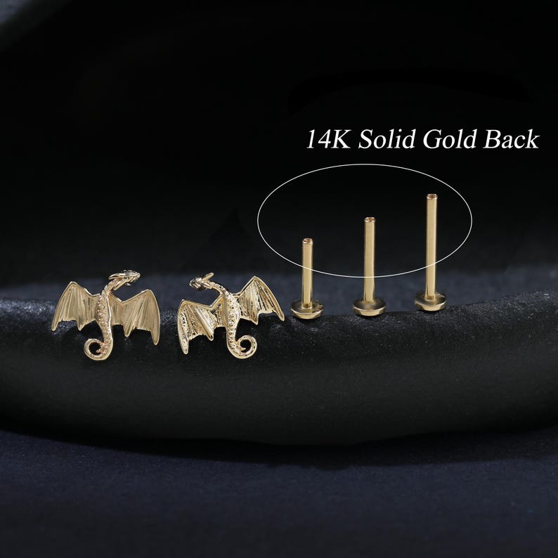 Puede incluir: Pendientes de drag&oacute;n dorados y tres postes de pendientes dorados. Los pendientes de drag&oacute;n tienen alas detalladas y un cuerpo curvado. El texto "14K Solid Gold Back" es visible en la imagen.