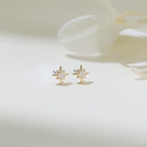 May include: A pair of gold star-shaped earrings with a small clear stone in the center of each star.