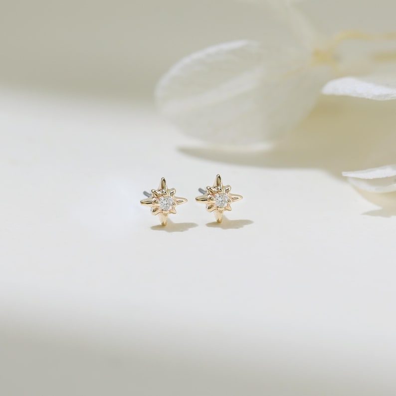 May include: A pair of gold star-shaped earrings with a small clear stone in the center of each star.