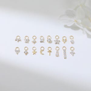 Puede incluir: Una colecci&oacute;n de colgantes dorados con varios dise&ntilde;os, incluyendo estrellas, flores y cruces. Cada colgante est&aacute; adornado con peque&ntilde;as gemas transparentes. Los colgantes est&aacute;n dispuestos sobre una superficie blanca.