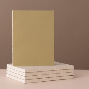 Könnte beinhalten: Ein senffarbener Planer mit den Worten "EVERYDAY PLANNER" auf dem Einband. Der Planer ist auf einem Stapel weißer Notizbücher gestapelt. Der Hintergrund ist einfarbig braun.