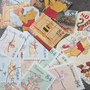 以下が含まれることがあります： くまのプーさんと仲間たちが描かれた、日本のヴィンテージ切手のコレクション。プーさん、ピグレット、ティガーなどのキャラクターが様々なポーズで描かれており、82と84の額面が表示されています。