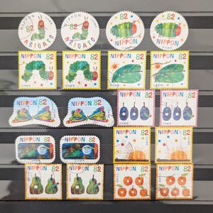 以下が含まれることがあります： カラフルな日本の切手のコレクション。 幼虫、蝶、果物、日の出のイラストが描かれています。 切手には「NIPPON 82」と「ARIGATO」の文字が記されています。