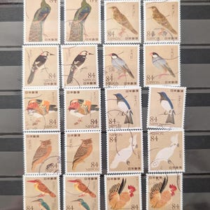 以下が含まれることがあります： 様々な鳥が描かれた、日本のヴィンテージ切手のコレクション。各切手は茶色の背景に、鳥の精巧なイラストと数字「84」が印刷されています。「NIPPON」の文字も各切手に印刷されています。
