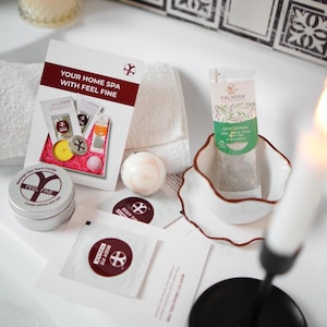 May include: A home spa kit with a white towel, a brochure with the text "YOUR HOME SPA WITH FEEL FINE", and various spa products. Includes a tin of "FEEL FINE" massage spa hand candle, bath bombs, and tea.