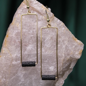 Puede incluir: Un par de pendientes de oro con detalles de roca volcánica negra. Los pendientes son de forma rectangular y tienen un diseño simple y minimalista.