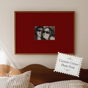 May include: A framed photo print featuring two people wearing sunglasses, set against a deep red background. The frame is a warm brown color. A white stamp-shaped graphic with the text "Custom Colour Photo Print" is in the lower right corner.