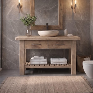 May include: A light brown wooden bathroom vanity featuring two drawers with metal handles, an open slatted bottom shelf holding folded white towels, and a round stone vessel sink centered on the top surface beneath a wooden mirror.