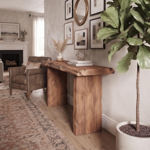Op de afbeelding: Een rechthoekige sidetable gemaakt van natuurlijk hout met een blad met een natuurlijke rand en twee dikke, plaatvormige poten. De tafel heeft een opvallende houtnerftextuur en een warme bruine afwerking, geplaatst tegen een muur in een woonruimte.