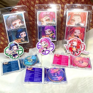 Op de afbeelding: Meerdere merchandise-artikelen met anime-personages. De items bevatten doorzichtige plastic cases met karakterkunst, cd's en karakterstickers. Het kleurenpalet omvat roze, paars, blauw en rood. De tekst "ZOEY LIMITED EDITION" is zichtbaar.