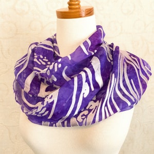 May include: A purple and white silk scarf with a wavy pattern. The scarf is draped over a mannequin's neck.