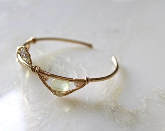 Pode incluir: Um bracelete de fio dourado com uma gema verde clara e cristais transparentes.