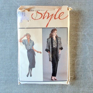 May include: A vintage sewing pattern envelope featuring two women's outfits. The first outfit is a black and white patterned blouse with a black wrap skirt. The second outfit is a black and white patterned jacket with black pants. The envelope is labeled "Style" in red cursive.