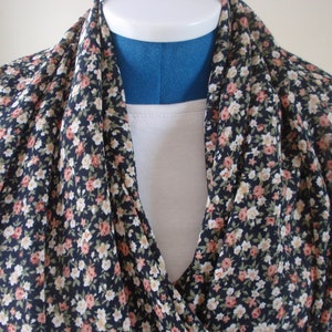 May include: A black floral scarf with small white and pink flowers. The scarf is draped around a mannequin's neck.