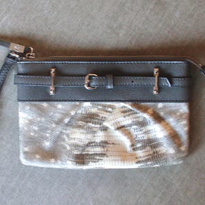 May include: A rectangular clutch with a wrist strap. The top section is dark gray with silver-tone hardware, including a buckle and two decorative bars. The bottom section has a snakeskin pattern in shades of gray and white.