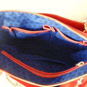 Pu&ograve; includere: Vista interna di una borsa rossa con cerniera dorata. L'interno &egrave; blu con un motivo a pois neri e ha diverse tasche. La borsa ha una tracolla a catena dorata.