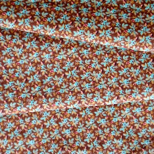 May include: Brown fabric with a repeating pattern of small blue flowers and leaves.