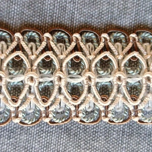 May include: Close-up of a decorative trim with a repeating pattern of brown, white, and light blue. The trim is made of woven fabric and has a delicate, intricate design.