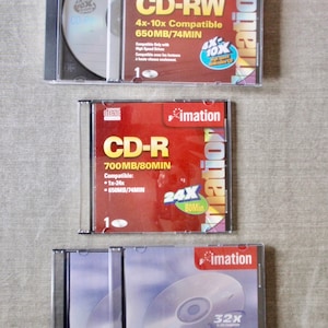 May include: Three packs of blank CD-R and CD-RW discs from the brand Imatation. The top pack is red and says "CD-RW 4x-10x Compatible 650MB/74MIN". The middle pack is red and says "CD-R 700MB/80MIN Compatible: 1x-24x 650MB/74MIN". The bottom pack is red and says "CD-R 80MIN/700MB".