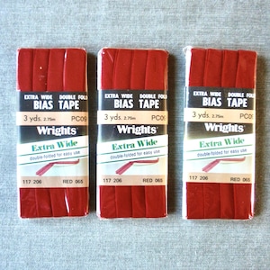May include: Three packages of red bias tape, each labeled "Extra Wide" and "Double Fold." The packaging includes the text "3 yds. 2.75m" and "Wrights." The color is "Red 065."