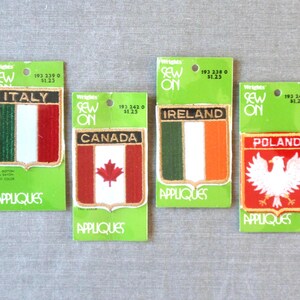 May include: Four sew-on appliqués featuring national flags: Italy, Canada, Ireland, and Poland. Each patch has a shield design with the country's flag colors and a white border. The patches are on green backing cards.