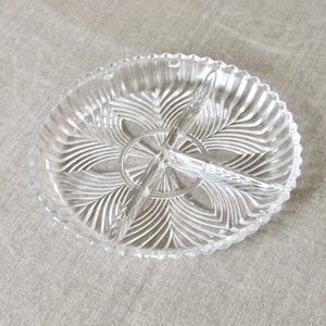 May include: Clear glass serving dish with three compartments. The dish has a scalloped edge and a central divider. The interior features a leaf-like pattern. Ideal for serving snacks or appetizers.