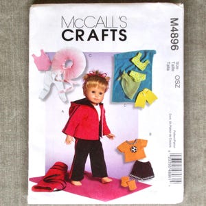 May include: A McCall's Crafts sewing pattern for doll clothes. The pattern includes instructions for a red jacket and black pants, a soccer uniform, and other outfits. The doll is wearing a red jacket and black pants.