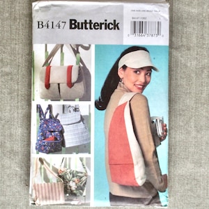 May include: Butterick B4147 sewing pattern featuring various bag designs. The pattern includes images of a messenger bag with red accents, a floral backpack, a striped tote, and a sling bag with a red panel. The model is wearing a sling bag.