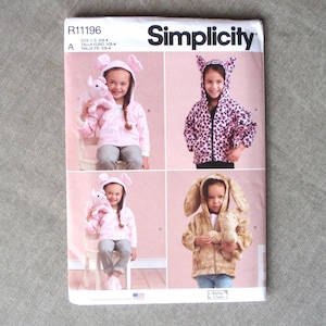 May include: Simplicity sewing pattern R11196 featuring children's bunny-themed jackets and hoodies. The pattern includes sizes 1/2-4. The image shows children wearing the finished garments in pink, leopard print, and brown faux fur.