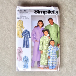 May include: Simplicity sewing pattern R11185 for robes. The pattern features illustrations of robes in yellow, blue, pink, and blue. The cover shows a family wearing robes in various colors, including green, purple, and green with white polka dots. The text reads "@Home easy-to-sew."