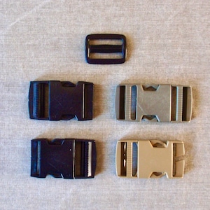 May include: An assortment of buckles in various styles and colors. The image shows a black rectangular buckle with two slots, two black side-release buckles, and two side-release buckles in silver and tan. These buckles are likely used for straps or belts.