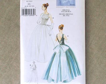 Op de afbeelding: Een vintage Vogue patroonpakket, V8729, met illustraties van elegante baljurken. Het pakket toont een vrouw in een witte jurk met handschoenen en een vrouw in een blauw-witte jurk met een grote strik. Het pakket is wit met tekst.