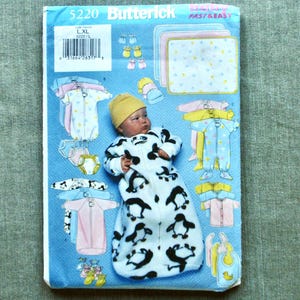 May include: A Butterick sewing pattern package, size L/XL, featuring a baby doll in a penguin-patterned sleep sack. The package includes illustrations of baby clothes in pastel colors. The text "FAST & EASY" is visible.