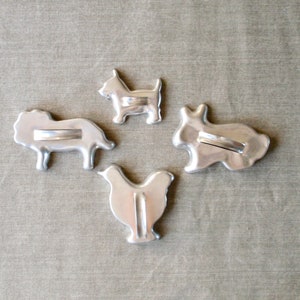 May include: Four metal cookie cutters shaped like a lion, a dog, a chicken, and a rabbit. The cutters are silver and have a smooth, shiny finish.