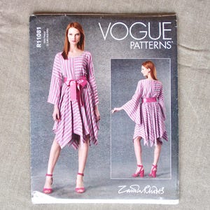May include: Vogue Patterns sewing pattern featuring a pink and white striped dress with a matching belt. The pattern cover includes a full-length image of the dress and a smaller image of the dress from a different angle. The Vogue Patterns logo is visible.
