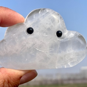 Könnte beinhalten: Eine weiße Kristallwolke mit einem geschnitzten Smiley-Gesicht und schwarzen Augen. Die Wolke ist glatt und poliert.